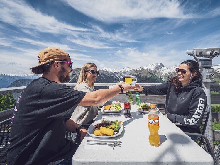 Drei Freunde stossen an und freuen sich auf Ihr Mittagessen auf der Sonnenterrasse Jatzmeder. | © Davos Klosters Mountains