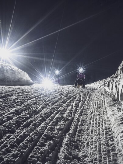 Mädchen mit Taschenlampe schlittelt auf der Nachtpiste hinunter. | © Davos Klosters Mountains